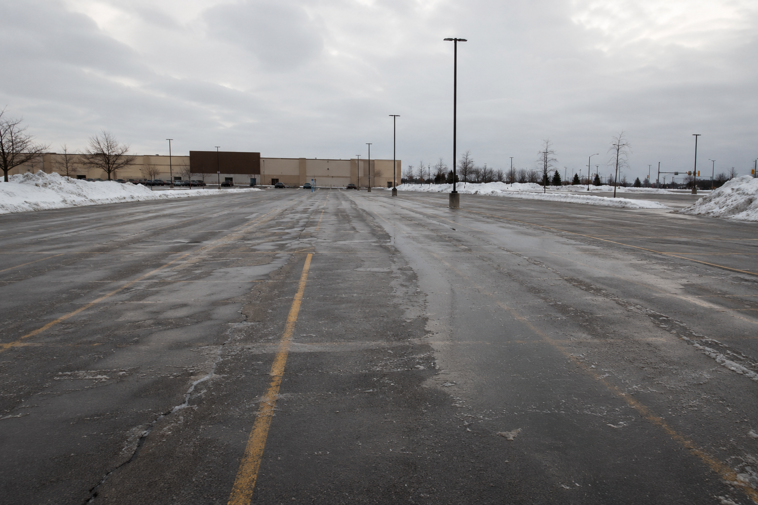 Large retail parking lot cleared to wet asphalt with snow piled along the edges