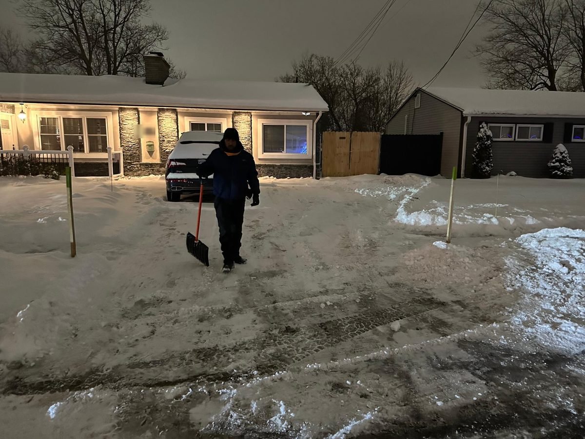 Crew member with a shovel clearing a residential driveway after dark
