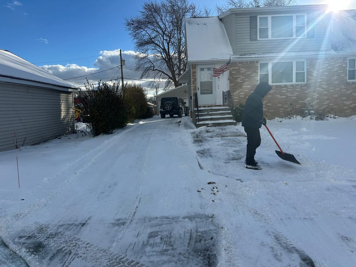 Crew member hand-shovelling the drive beside a home's front steps on a sunny winter day