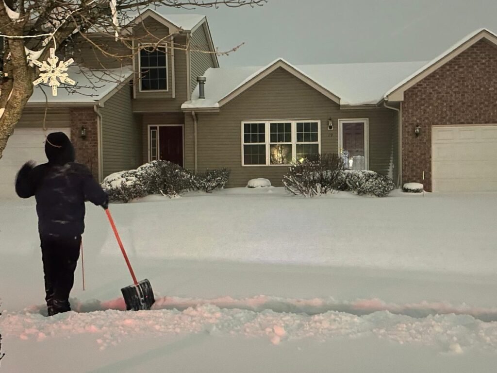 Crew member shovelling deep snow in front of a townhouse garage
