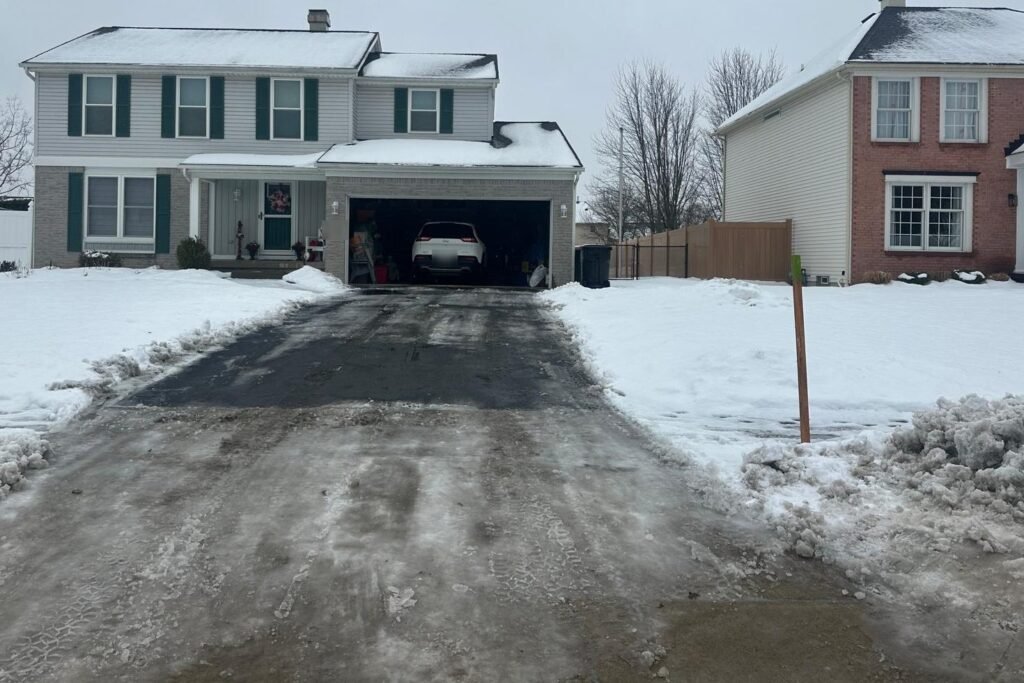 Two-car residential driveway plowed full width, with a snow stake marking the edge at the apron