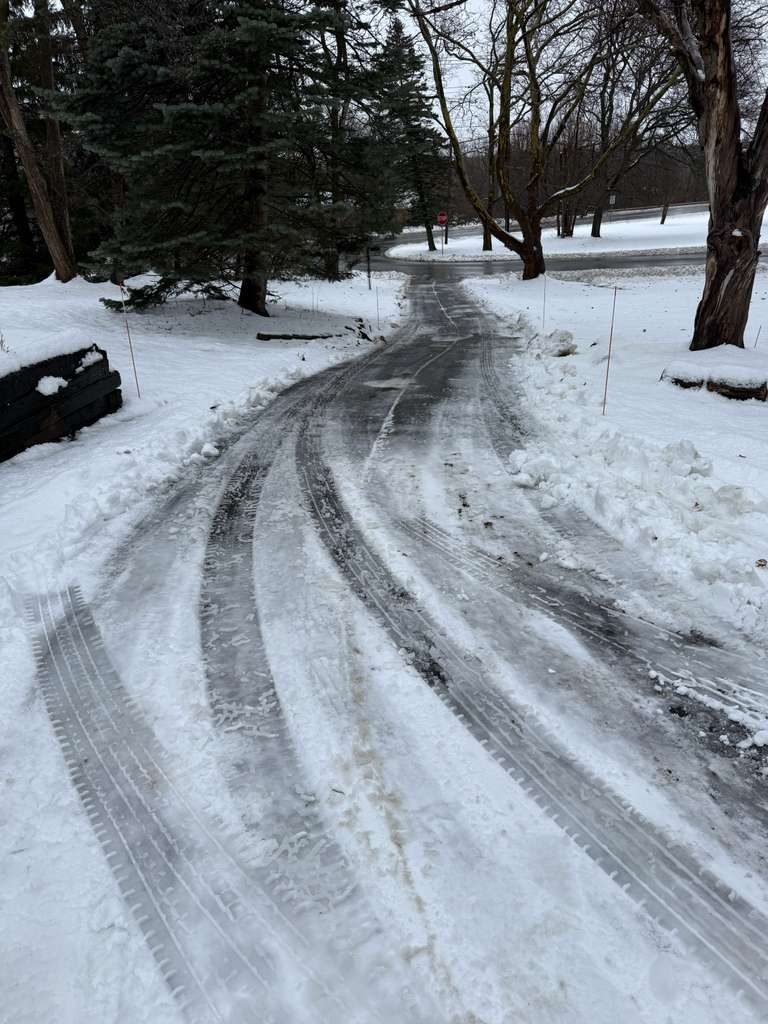 Curved residential driveway plowed between orange marker stakes in Orchard Park, NY