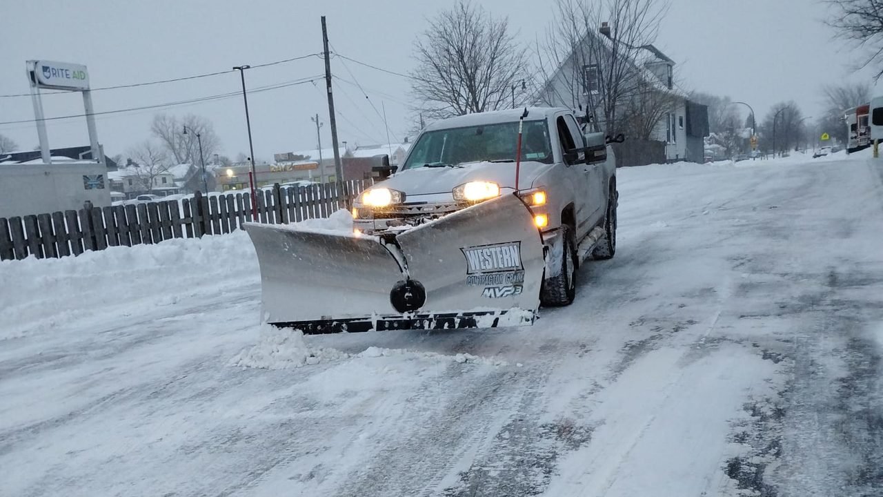 Pickup truck with a snow plow clearing a commercial parking lot