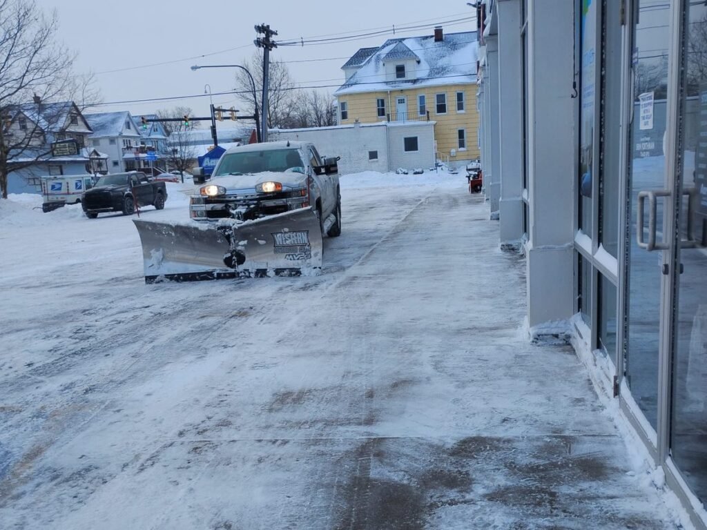 Plow truck clearing the lot along a row of storefronts